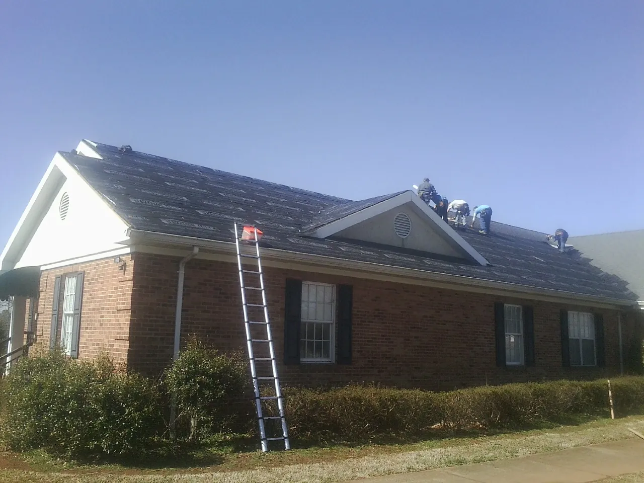 Crew tearing shingles off a brick ranch roof with a ladder set — Emergency Roof Repair work by our crew in Skyforest