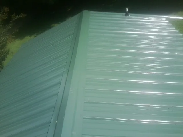 New green metal panels meeting at the ridge of a roof — Flat Roof Repair work by our crew in Skyforest