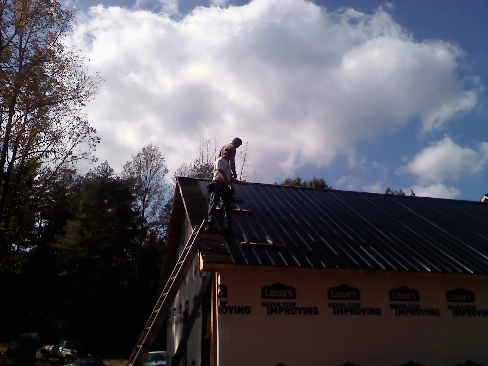 Roofer fastening dark metal panels high against a cloudy sky, from a Roof Inspection job in Skyforest