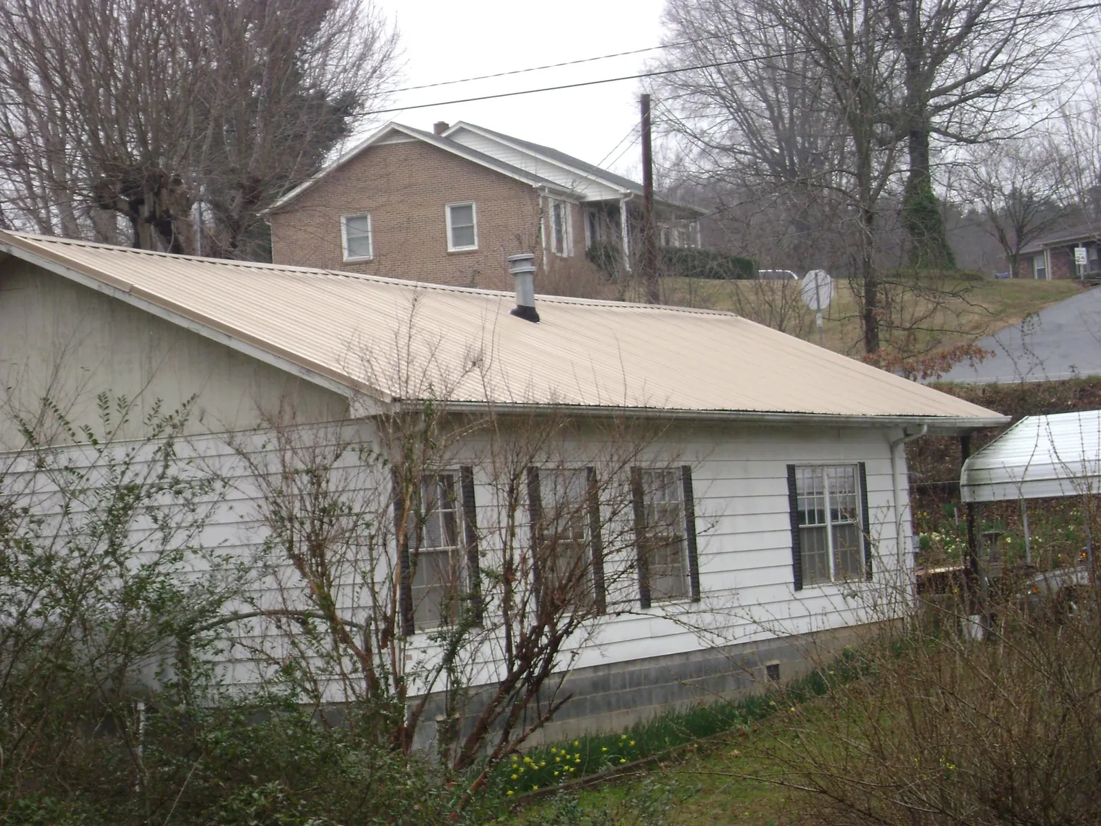 Tan metal roof on a white sided house set into a hillside — Commercial Roofing by Roofing Brothers in Skyforest