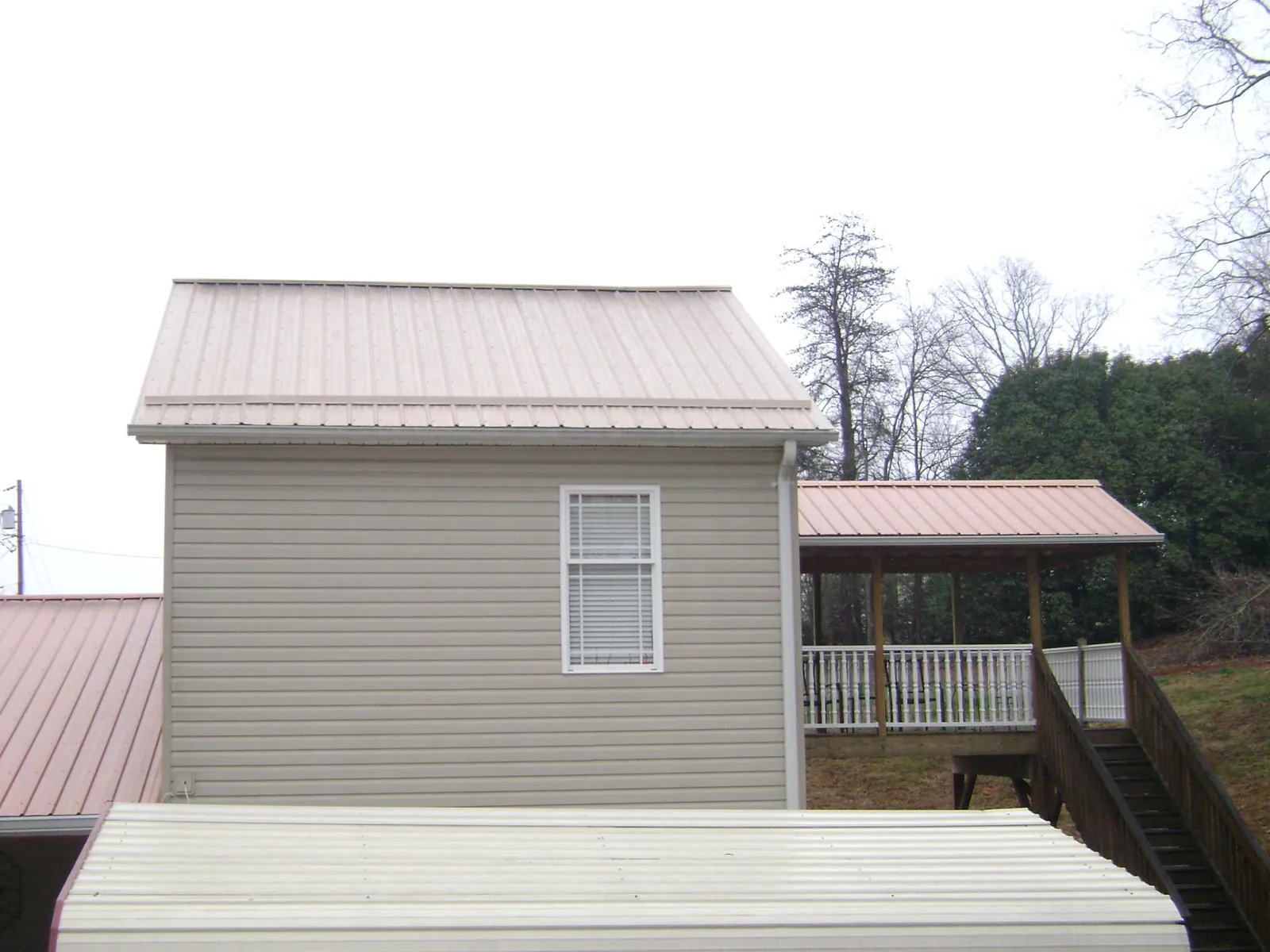 Tan metal roofs on a two story addition and attached porch, from a Roof Replacement job in Skyforest